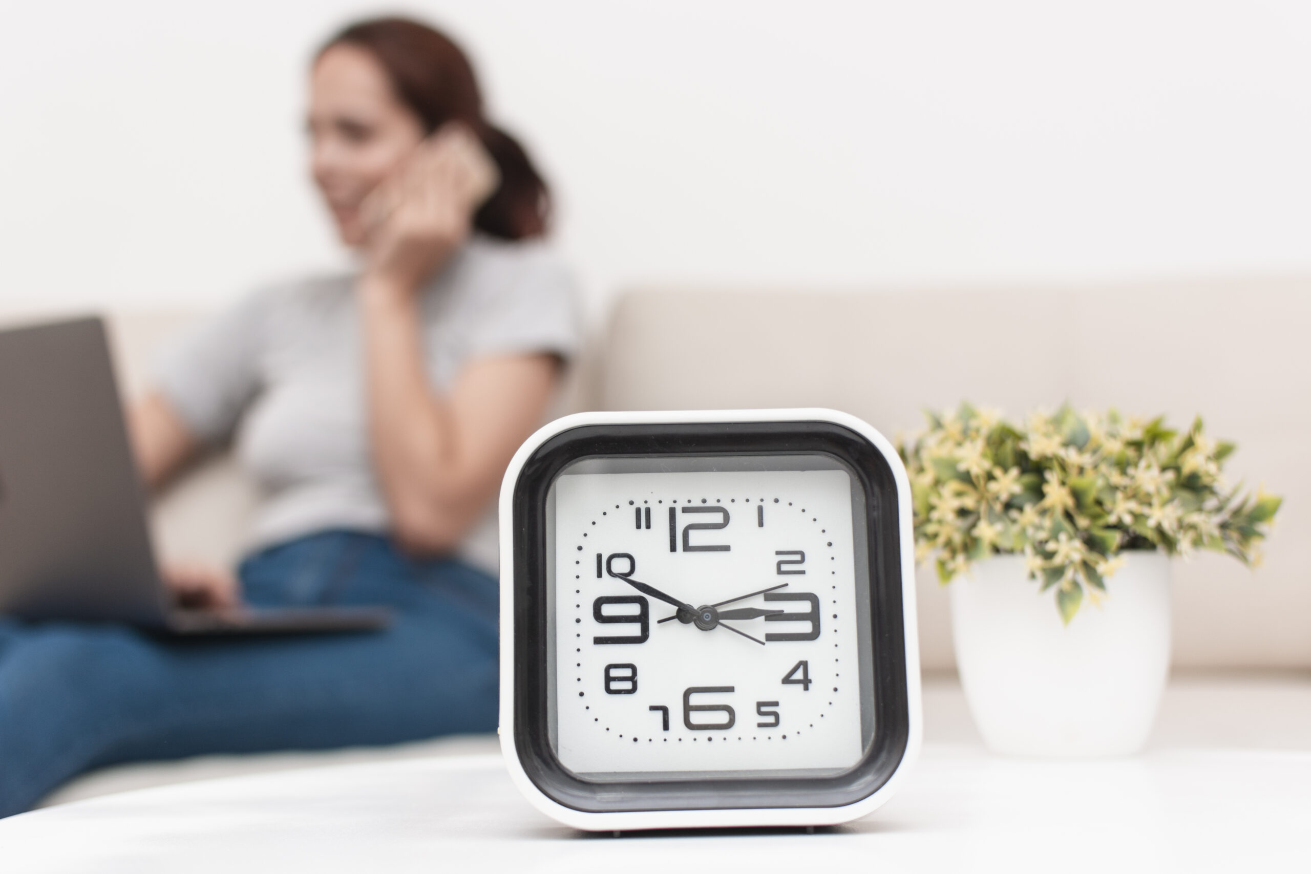 "Mujer distraída por una llamada telefónica, con reloj marcando el paso del tiempo y simbolizando la procrastinación."