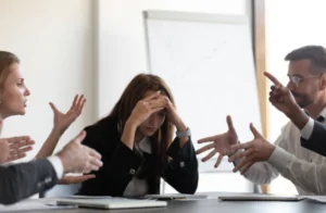 Mujer con estrés laboral mientras sus compañeros gesticulan, imagen que ilustra el impacto del burnout en los equipos y cómo las Barras de Access pueden ayudar